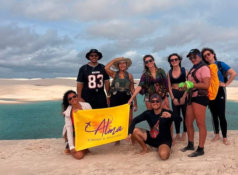 Grupo de viajantes da Alma nos Lençóis Maranhenses, segurando a bandeira da Alma
